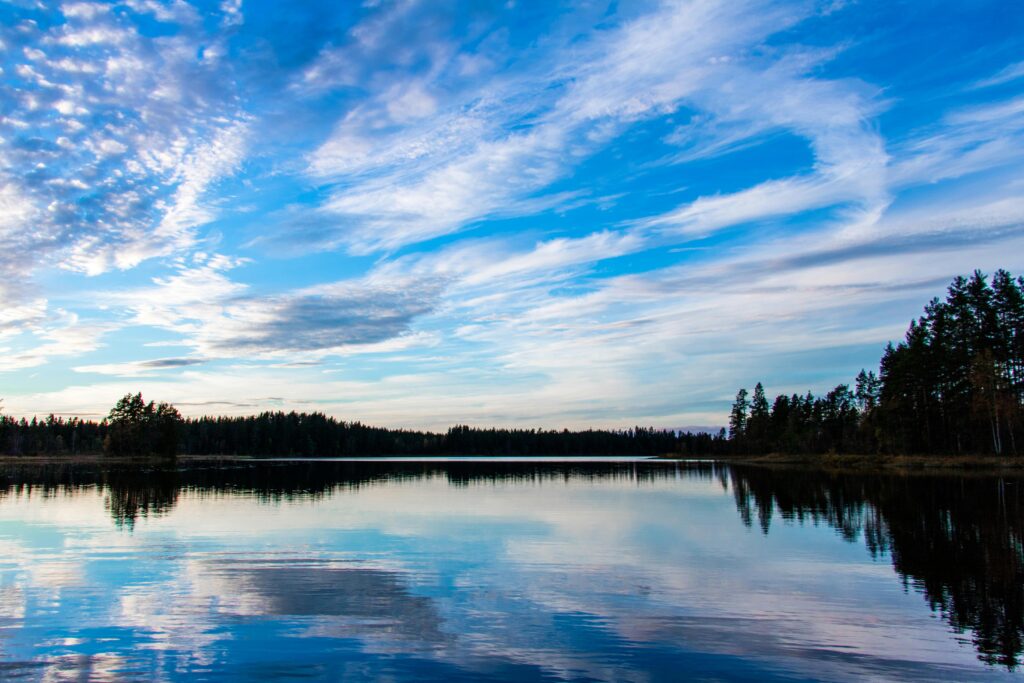A tranquil lake with a forest reflection under a vibrant blue sky.
